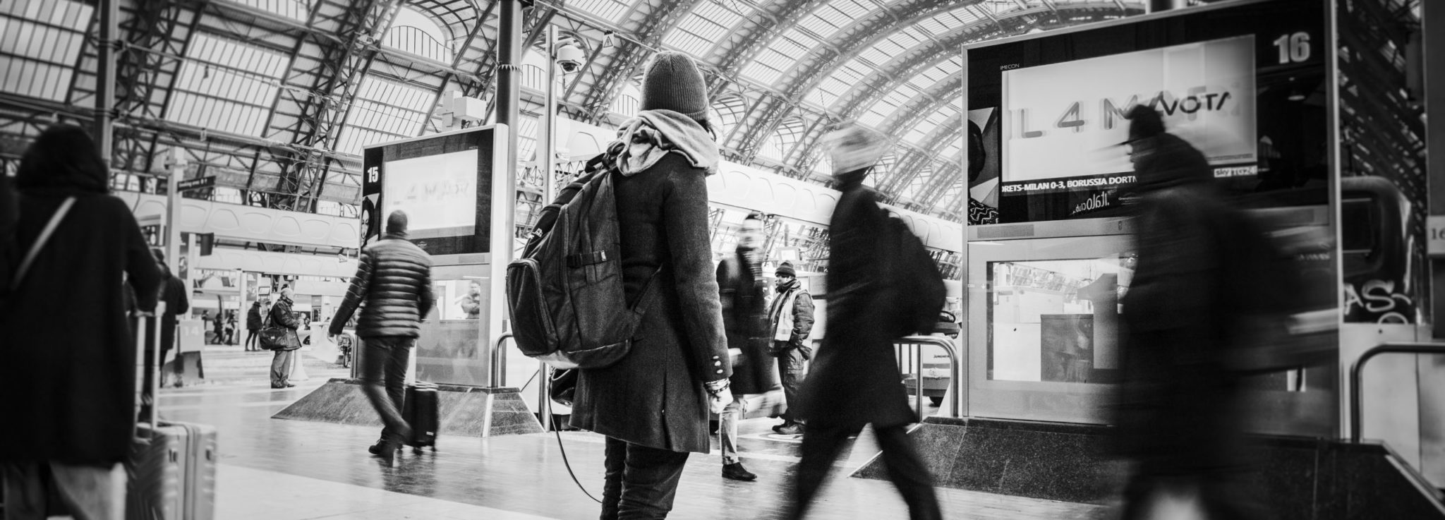Person looking at tv screen in busy train station - representing a setting to avoid risks of cultural differences in communication