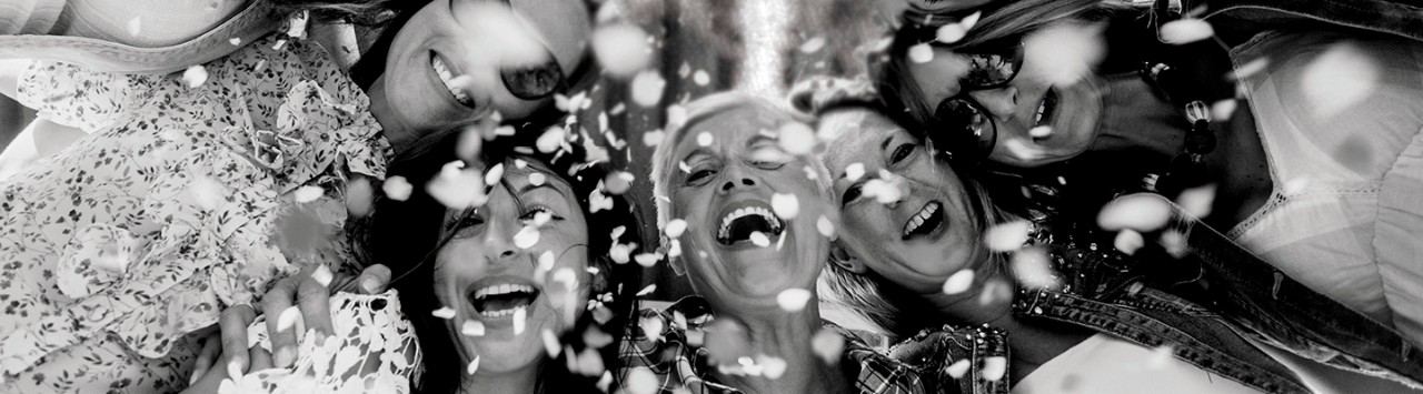 A group of women smiling and laughing look up through confetti.